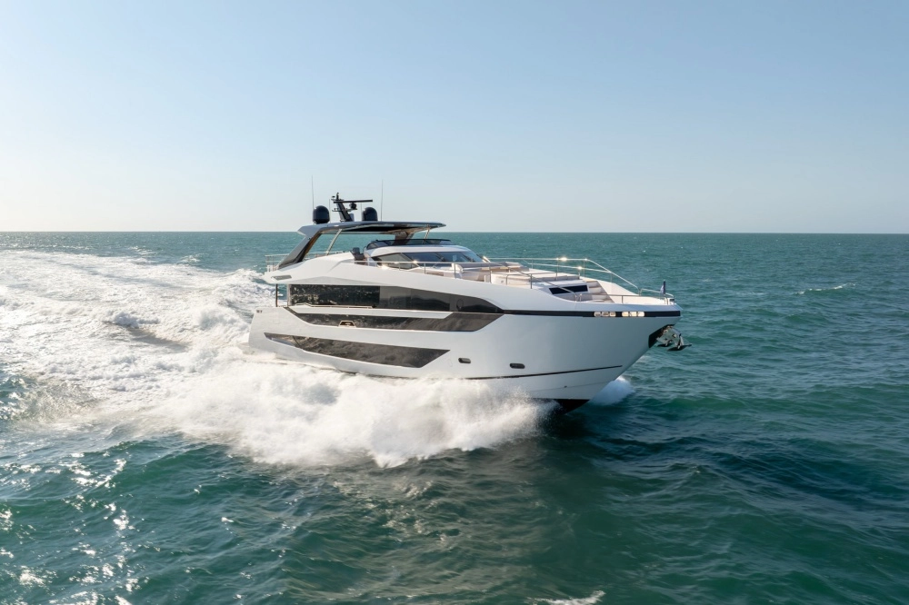 Açık denizde, beyaz gövdesi ve modern hatlarıyla dikkat çeken İngiliz yapımı Sunseeker Manhattan 94 süper yatı, arkasında güçlü bir köpük izi ve dalgalar bırakarak ileri doğru hızla yol alırken, gökyüzü berrak ve deniz masmavi.