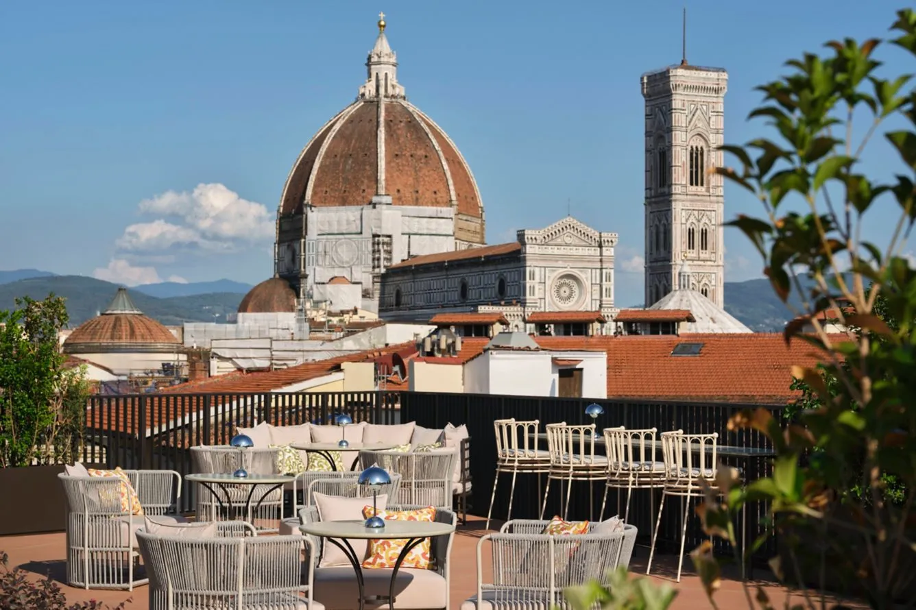 Florence'da bulunan W Hotel'in çatı terasından, modern ve açık renkli hasır dokulu oturma grupları ve masalarla döşenmiş alanda, Floransa Katedrali'nin ünlü Brunelleschi Kubbesi ve Giotto'nun Çan Kulesi'nin nefes kesici tarihi manzarasına karşı, güneşli bir günde keyifli anlar sunan şık bir mekan.
