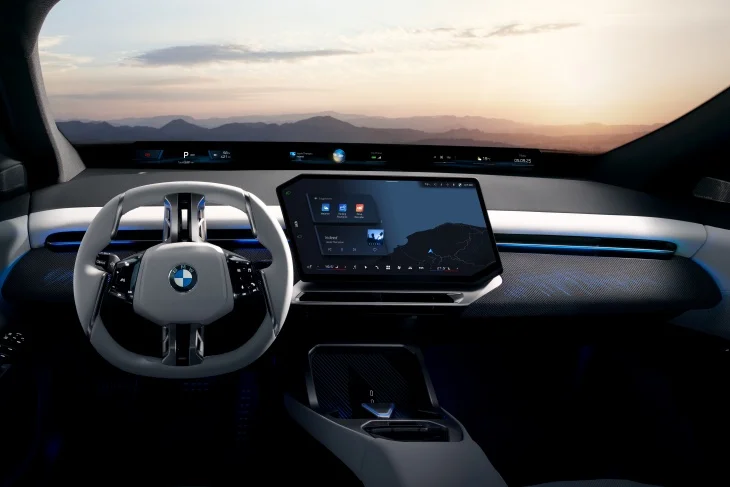 Yeni BMW iX3'ün minimalist ve dijital odaklı iç tasarımını gösteren bu geniş açılı görselde, açık renkli direksiyon, geniş merkezi bilgi-eğlence ekranı ve Neue Klasse felsefesini yansıtan ön cam boyunca uzanan BMW Panoramic Vision dijital gösterge paneli, dağ manzaralı bir gün batımı eşliğinde elektrikli geleceği yansıtıyor.