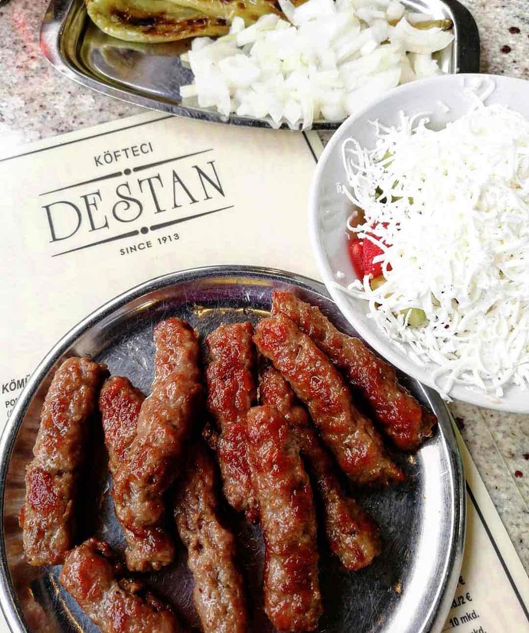 Üsküp'ün zengin tarihinden ve Balkan mutfağının köklü mirasından izler taşıyan Destan Köfte'den nefis parmak köfteler, yanında bol rendelenmiş peynirli taze salata ve doğranmış soğanla sunuluyor, şehrin otantik lezzet duraklarından birine davet niteliğinde.