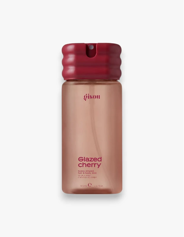 Beyaz arka plan üzerinde, koyu kırmızı, tırtıklı bir kapağı ve üzerinde büyük harflerle Glazed cherry yazan şeffaf, bal rengi bir Gisou Glazed Cherry Bal İnfüzyonlu Saç ve Vücut Spreyi şişesi görülüyor.