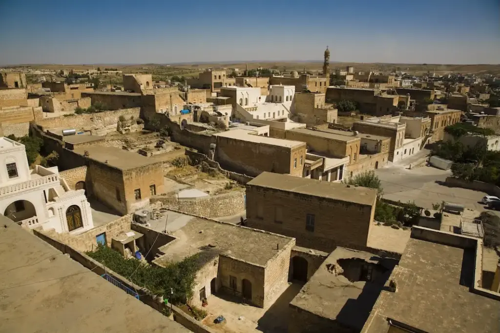 Yüksekten çekilmiş bu geniş açılı görüntüde, Mardin'in kendine özgü sarı kalker taşından yapılmış, kadim mimarisiyle öne çıkan taş evleri ve aralarından kıvrılan dar sokakları, ufukta uzanan uçsuz bucaksız Mezopotamya Ovası'yla bütünleşerek şehrin eşsiz dokusunu ve Mardin'de gezilecek yerlerin büyülü atmosferini sergiliyor.