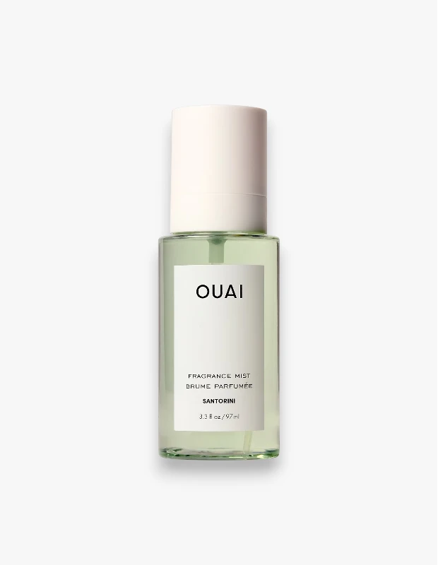Açık yeşil sıvı içeren, beyaz kapaklı ve şeffaf dikdörtgen Ouai Fragrance Mist Santorini şişesi, üzerinde OUAI markası, FRAGRANCE MIST, BRUME PARFUMÉE ve SANTORINI yazılarıyla detaylandırılmış beyaz bir etiketle beyaz arka plan üzerinde duruyor.