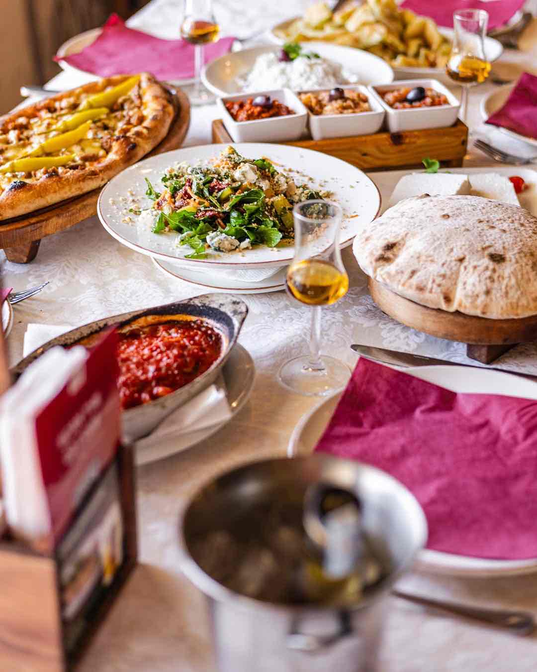 Beyaz masa örtüsüyle donatılmış zengin Üsküp sofrasında, közlenmiş biberli pide, taze yeşillik ve peynirle hazırlanmış salata, güveçte pişmiş bir sos, yanında geleneksel Makedon içkisi rakija olduğu anlaşılan kadehlerle birlikte iştah açıcı birçok Balkan lezzeti sergileniyor.