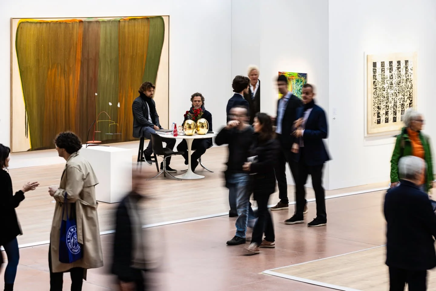 Art Basel Paris'te, geniş ve ışıklı bir sergi salonunda, farklı yaş ve tarzlardaki çok sayıda ziyaretçi, soyut ve figüratif tabloların yanı sıra modern heykelleri içeren çeşitli çağdaş sanat eserlerini dikkatle inceliyor ve etkinlik alanında dolaşarak sanatın nabzını tutuyor.