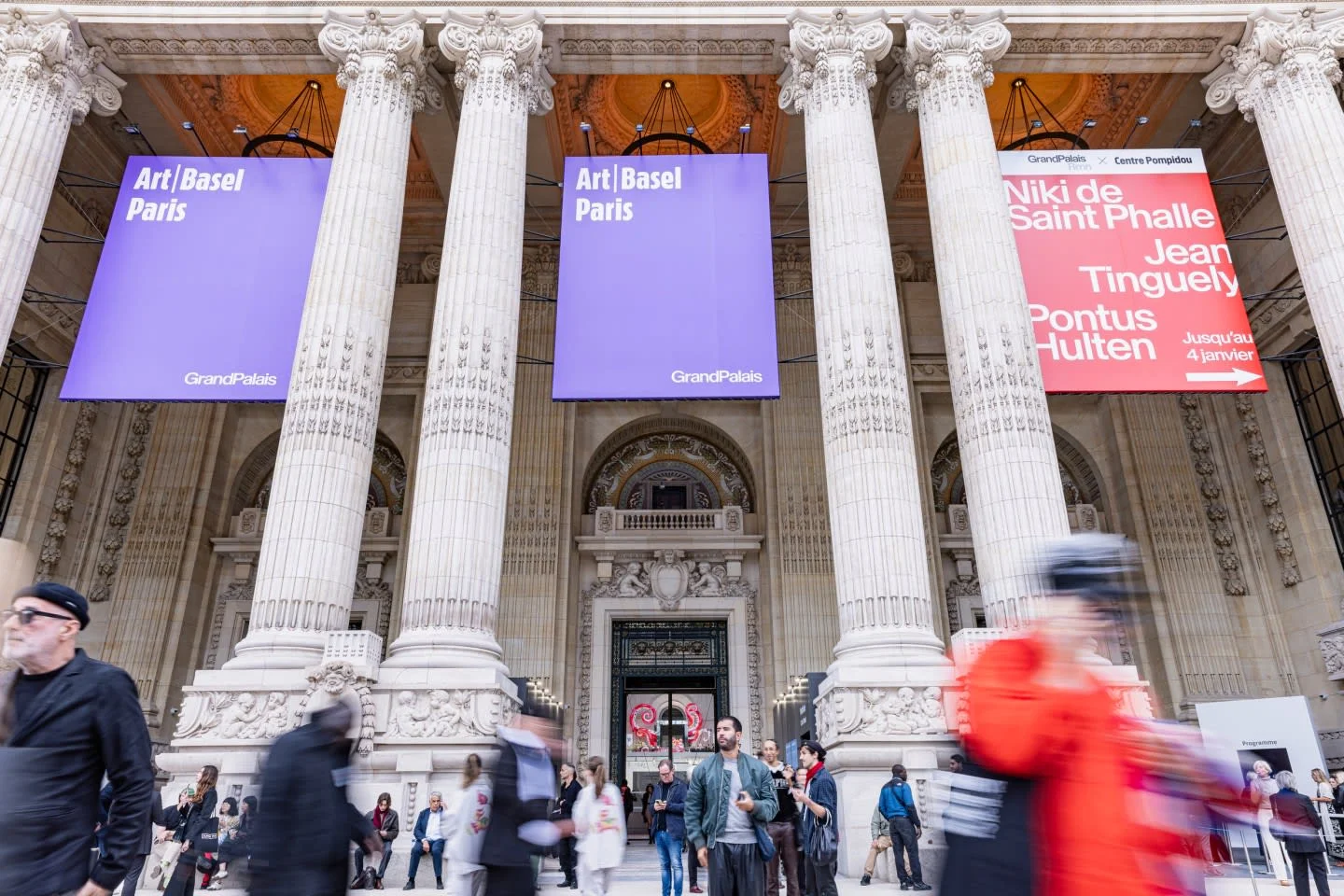 Art Basel Paris'ten bir görünüm sunan bu fotoğraf, modern sanat eserlerinin sergilendiği geniş bir salonda gezen, heykelleri, büyük boyutlu tabloları ve diğer çağdaş enstalasyonları dikkatle inceleyen ziyaretçilerin oluşturduğu canlı ve hareketli bir atmosferi detaylandırıyor.
