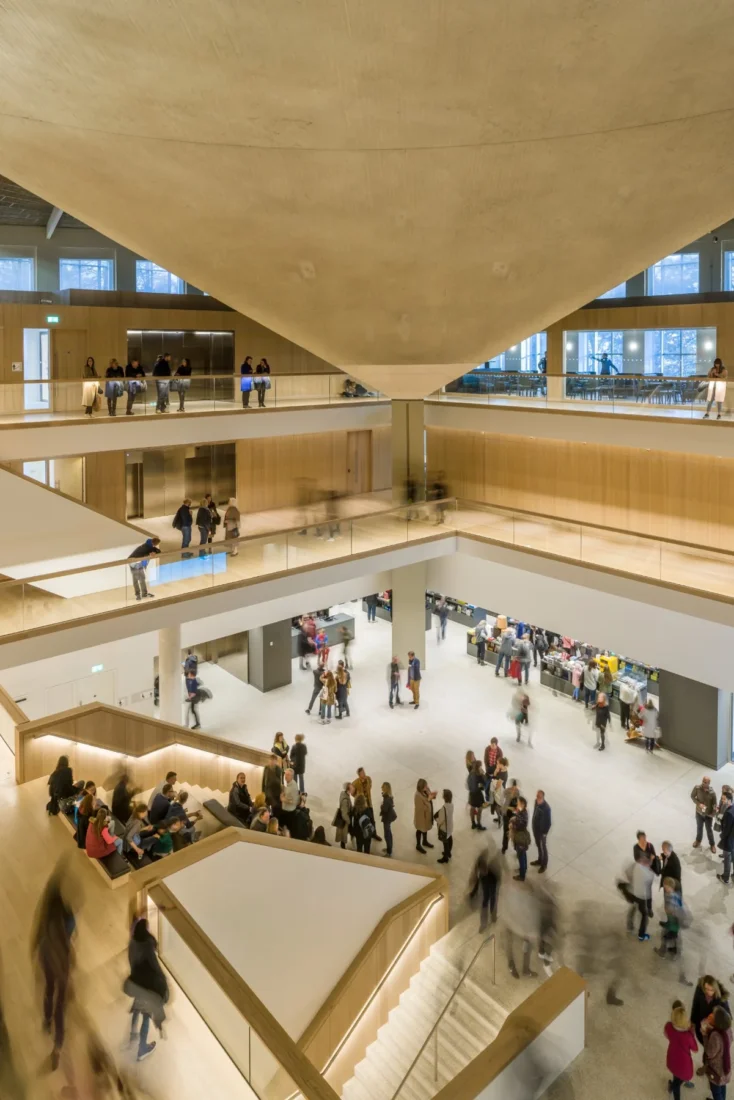 Modern bir iç mekanda, arkasında soyut bir sanat eserinin bulunduğu beyaz bir duvarın önünde duran gözlüklü ve takım elbiseli Gareth Gardner, profesyonel bir duruş sergileyerek fotoğrafçı kimliğini ve mimari fotoğrafçılık alanındaki uzmanlığını yansıtıyor.