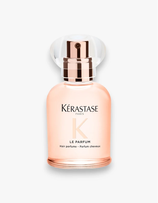 Beyaz bir zeminde, üstünde Kérastase Paris logosu ve LE PARFUM yazısı bulunan, şeftali tonlarında oval bir saç parfümü şişesi, rose altın renkli püskürtücüsü ve şeffaf, dalgalı formdaki kapağıyla ürüne modern ve şık bir görünüm katıyor.