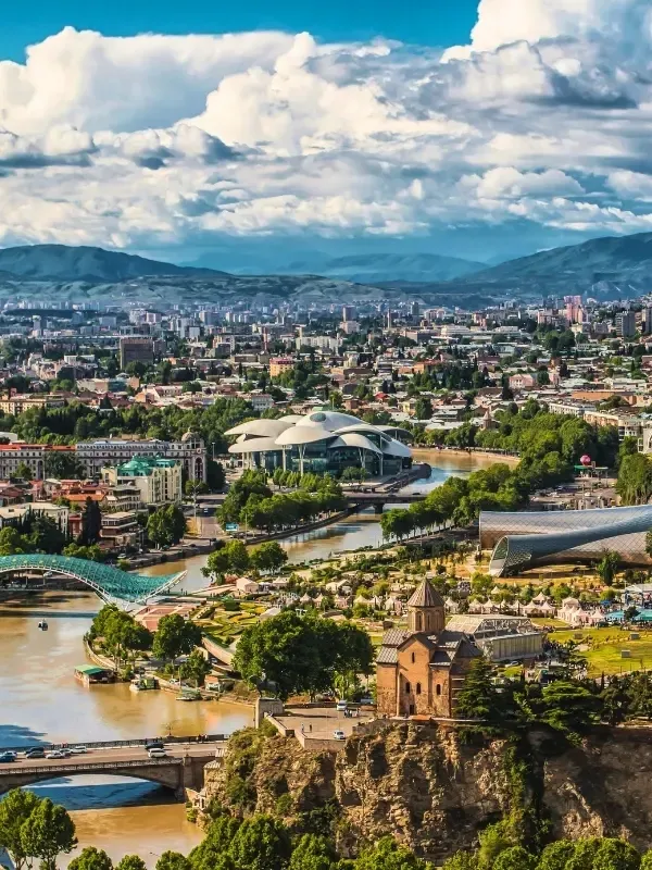 Tiflis'in Kura Nehri üzerinde, antik Metekhi Kilisesi'nin kayalık bir yamaçta yükseldiği, modern Barış Köprüsü'nün ise nehrin iki yakasını birleştirdiği bu geniş panoramik şehir manzarasında, yemyeşil ağaçlar, diğer köprüler ve uzak dağlar bulutlu gökyüzünün altında uzanıyor.