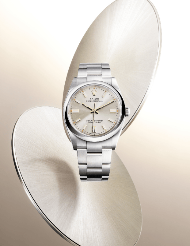 Altın ve krem tonlarında modern bir arka plan önünde sergilenen, şampanya kadranlı paslanmaz çelik Rolex Oyster Perpetual saat.