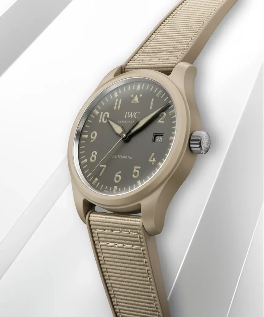 IWC kadran tasarımına sahip bej kasa ve NATO tarzı kayışlı otomatik pilot saatinin modern ürün çekimi; minimalist lüks ve dayanıklı saat tasarımı.