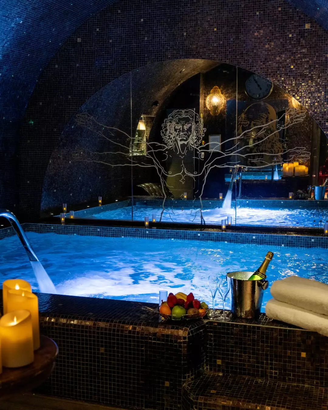 Kemerli tavanlı, loş ışıklı, taş benzeri bir mimariye sahip lüks kapalı spa alanında, köpüklü ve şelaleli iki büyük mavi aydınlatmalı havuzun önünde, şampanya kovası, düzenli katlanmış beyaz havlular, küçük bir meyve tabağı ve yanan mumlar bulunmaktadır.