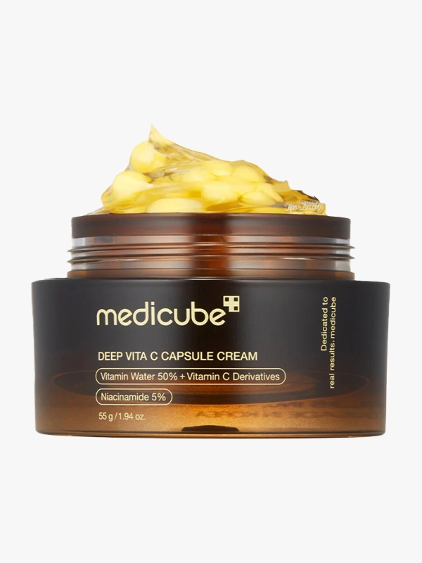 Amber rengi kapağı açık bir kavanozun içinden taşan, küçük açık sarı kapsüllerle zenginleştirilmiş şeffaf sarı renkli Medicube Deep Vita C Capsule Cream, cildi aydınlatıp tonunu eşitlemeye yardımcı olan, Niasinamid %5 ve Vitamin C Türevleri içeren hafif yapılı bir nemlendirici olarak sunuluyor.