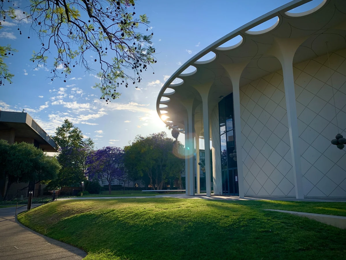 Caltech Kaliforniya Teknoloji Enstitüsü'nün yeşil alanlar ve ağaçlarla çevrili, akademik mimariye sahip etkileyici bir binası, güneşli bir günde kampüsün sakin ve bilimsel atmosferini vurgulayarak bilimin geleceğine ışık tutuyor.