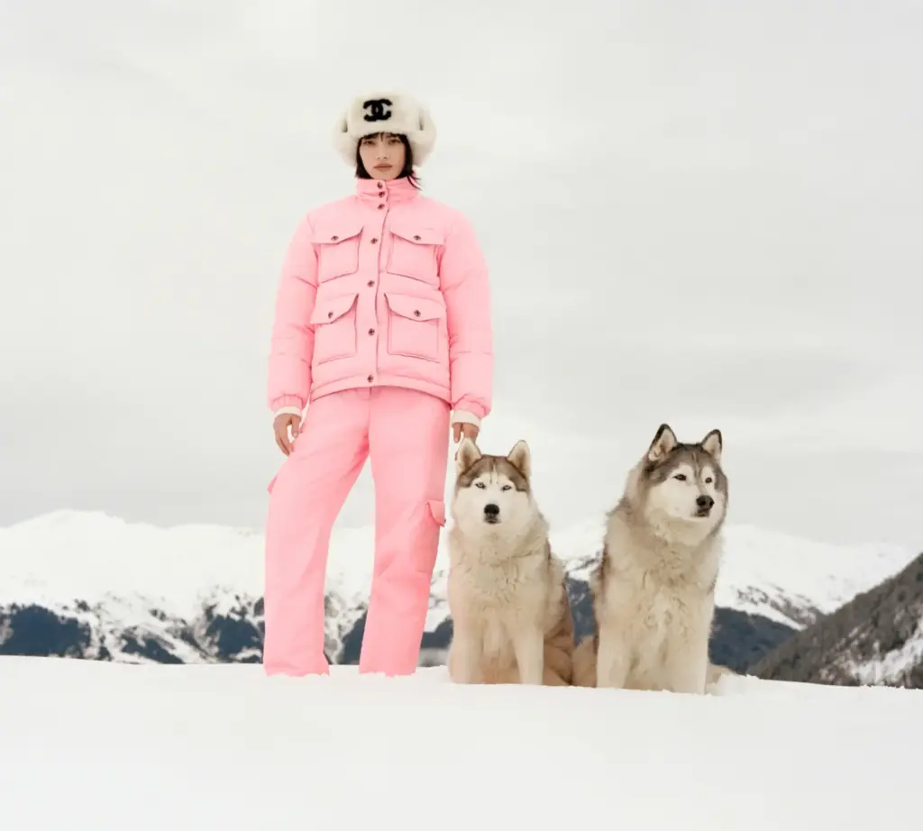 chanel kayak koleksiyonundan pembe kayak tulumu giyen ve iki sibirya kurduyla karlı bir ortamda poz veren model