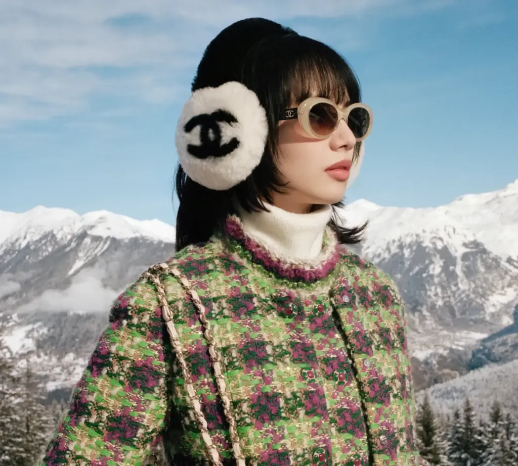 Karlı bir dağın önünde poz veren ve Chanel kayak koleksiyonundan Chanel logolu türlü kulaklık takan Asyalı model
