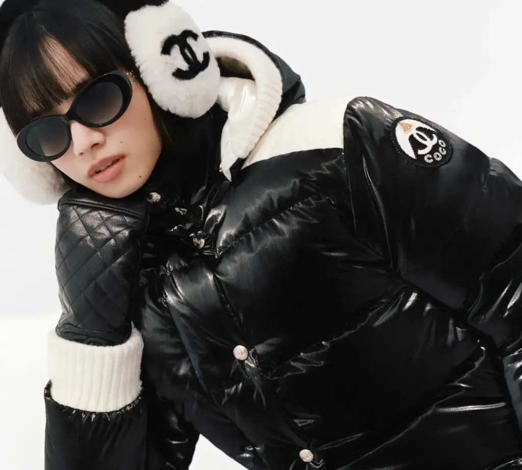 Chanel kayak koleksiyonundan Siyah kayak montu, siyah kar eldiveni ve beyaz tüylü Chanel logolu kulaklık takarak poz veren model