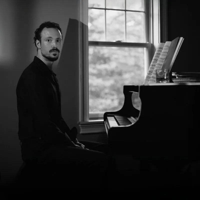 Piyanist Eric Christian, Türkiye'deki ilk performansına hazırlanırken sahnesinde koyu renk smokiniyle kuyruklu piyanosunun başında oturmuş, tuşların üzerinde duran elleri ve düşünceli yüz ifadesiyle klasik ve modern müziği harmanlayan duygusal bestelerini yansıtan bir anı canlandırıyor.