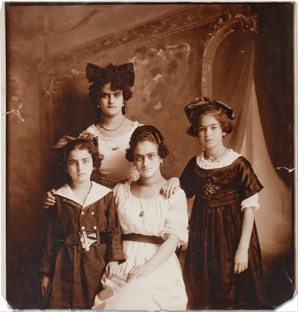 Sepya tonlu eski bir fotoğraf, sanatçı Frida Kahlo'nun ailesiyle birlikte stüdyoda çekilmiş gençlik yıllarından bir portreyi sergiliyor; ortada büyük bir fiyonklu ablası, sağda kahverengi elbiseli genç Frida, solda koyu renkli denizci tarzı elbiseli küçük kız kardeşi ve önde oturan diğer kız kardeşi ciddi ifadelerle objektife bakıyor.