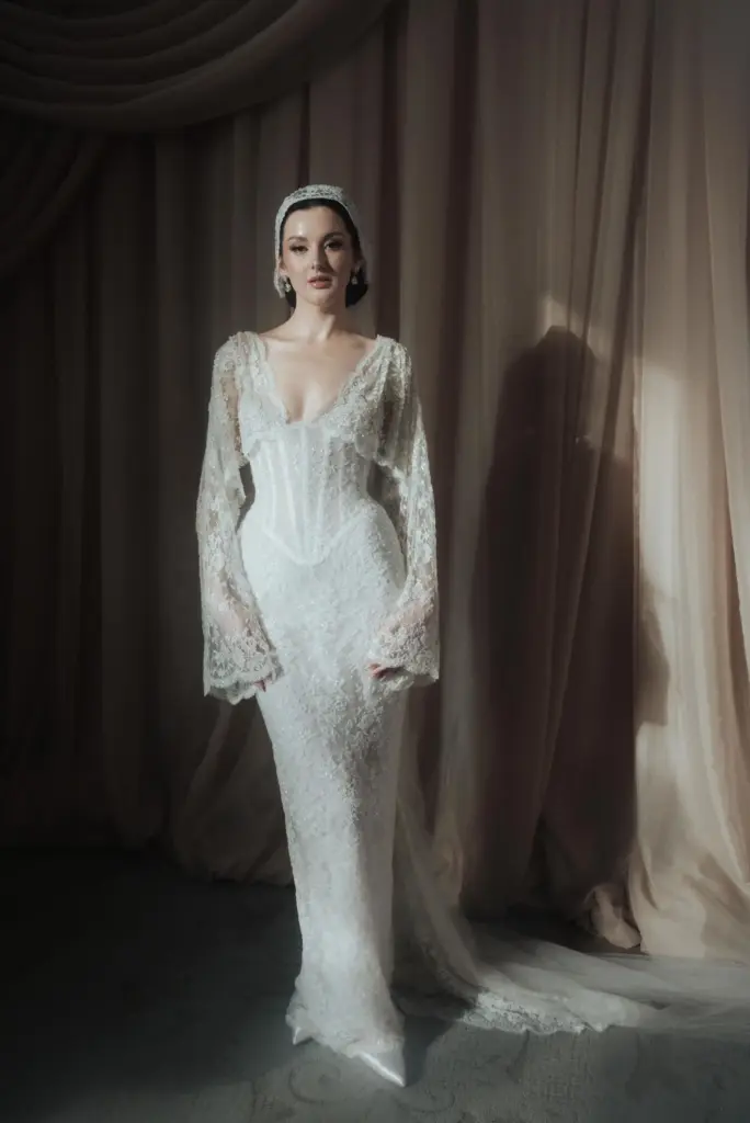 Dantel işlemeli korsaj detaylı, uzun kollu vintage esintili gelinlik giyen modelin dramatik ışık altında çekilmiş portresi.