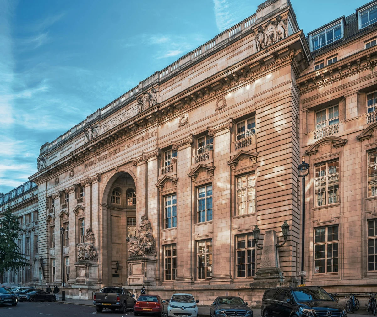 Londra'daki Imperial College'ın görkemli, tarihi mimarisiyle öne çıkan, detaylı taş işçiliğine sahip büyük binası, yemyeşil ağaçların ve berrak gökyüzünün altında bilgi ve bilimin simgesi olarak yükseliyor.