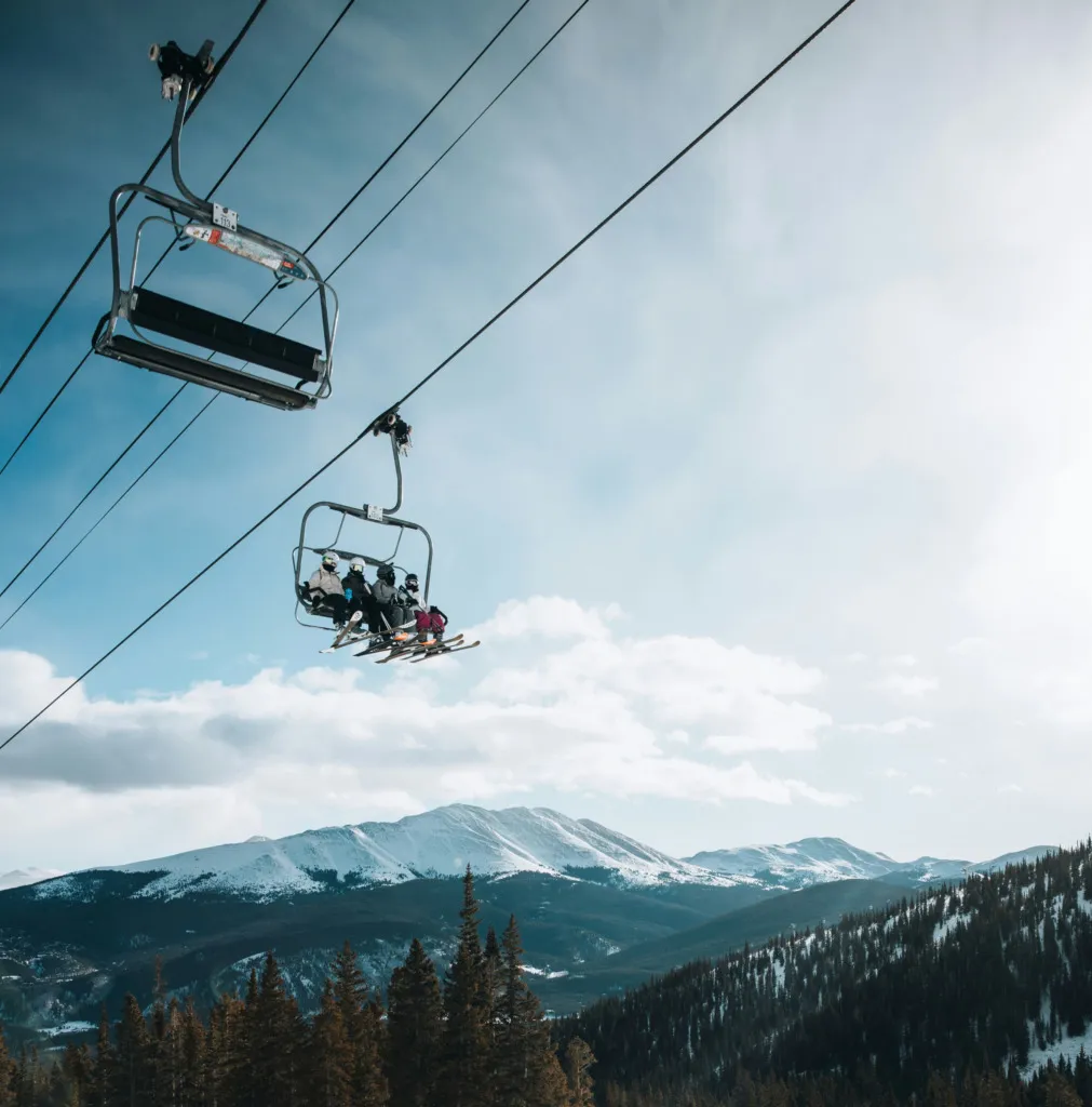 Dağ manzarası eşliğinde chairlift ile yukarı çıkan kayakçılar