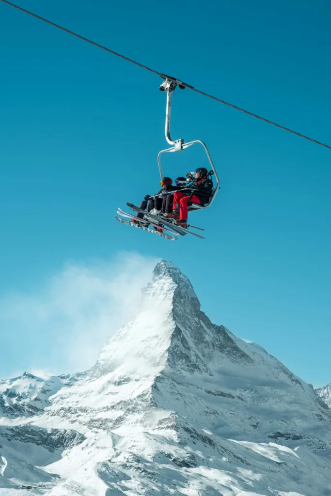Dağ zirvesi önünde ilerleyen chairlift ve kayakçılar
