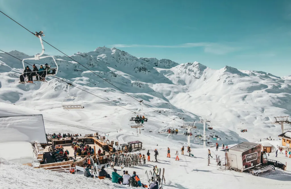 Dağ manzaralı kayak merkezinde ski lift, pistler ve kalabalık tesis alanı