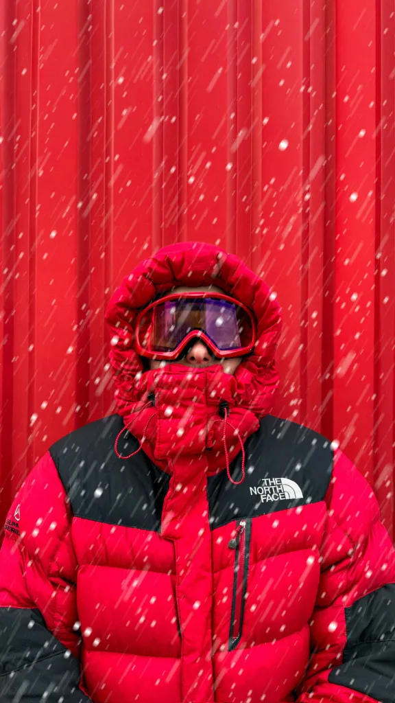 Karlı dağlarda kırmızı mont ve kaskıyla snowboard yapan sporcu