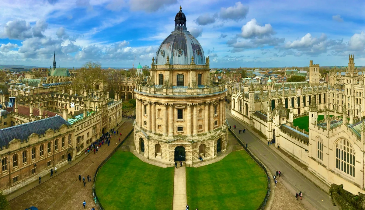 Oxford Üniversitesi'nin asırlık kampüsünden, tarihi Gotik mimarisiyle öne çıkan görkemli bir yapıyı gösteren bu geniş açılı fotoğraf, güneşli bir günde binaların detaylı taş işçiliğini ve yüksek kulelerini gözler önüne sererek üniversitenin zengin geçmişini ve prestijli akademik kimliğini vurguluyor.