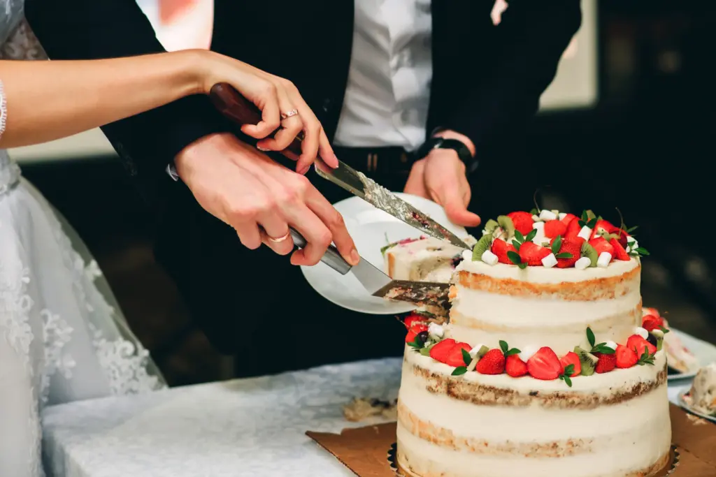 Düğün pastası kesme anı; gelin ve damat, çilek ve kivi süslemeli iki katlı pasta kesiyor, romantik düğün detayı