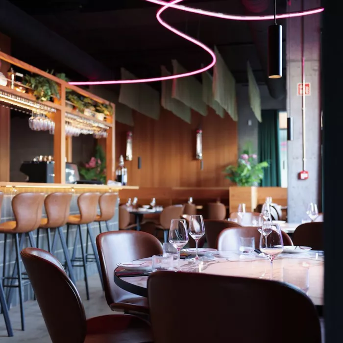 Reykjavik seyahat rehberi içinde yer alan şık bir restoranın iç mekanında, koyu renk tavanından sarkan pembe neon ışıklandırmanın aydınlattığı modern ahşap paneller, deri sandalyeler ve özenle hazırlanmış masalar göze çarpıyor.