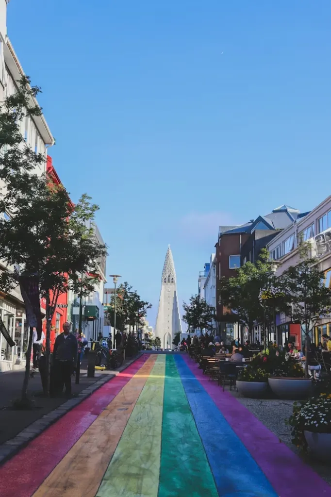 Güneşli bir günde Reykjavik şehir merkezindeki renkli Rainbow Street, Hallgrímskirkja Kilisesi'ne doğru uzanırken, yol boyunca sıralanmış hareketli kafeler ve butiklerle dolup taşıyor, bu ikonik görüntü Reykjavik Seyahat Rehberi'nin önemli duraklarından biri.
