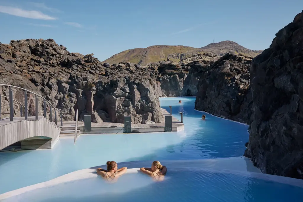 İzlanda'nın volkanik kaya oluşumlarıyla çevrili, süt mavisi sularıyla ünlü Blue Lagoon'da iki kadın ve diğer ziyaretçiler huzurla dinlenirken, Reykjavik seyahatlerinin termal deneyimini en güzel şekilde yaşıyorlar.