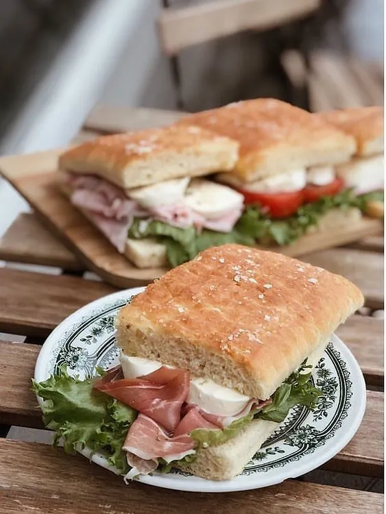 Ahşap bir masada sunulan, üzeri tuzlu focaccia ekmeği arasına bol yeşillik, ince dilimlenmiş kurutulmuş et ve mozzarella peyniriyle hazırlanmış iki iştah açıcı sandviç, Reykjavik seyahatinde tadılabilecek hafif öğle yemeği ve kafe lezzetlerini yansıtıyor.
