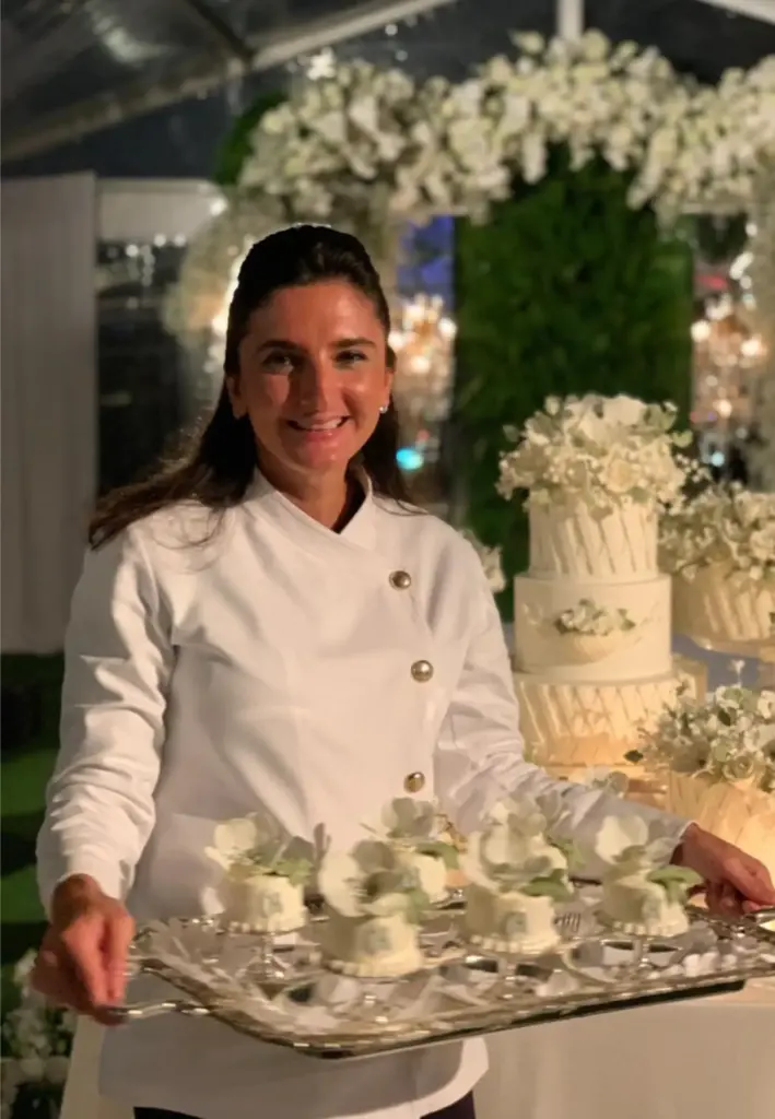 Sinem Ekşioğlu düğün pastalarının önünde. üzerinde cupcakeler bulunan tepsi tutuyor