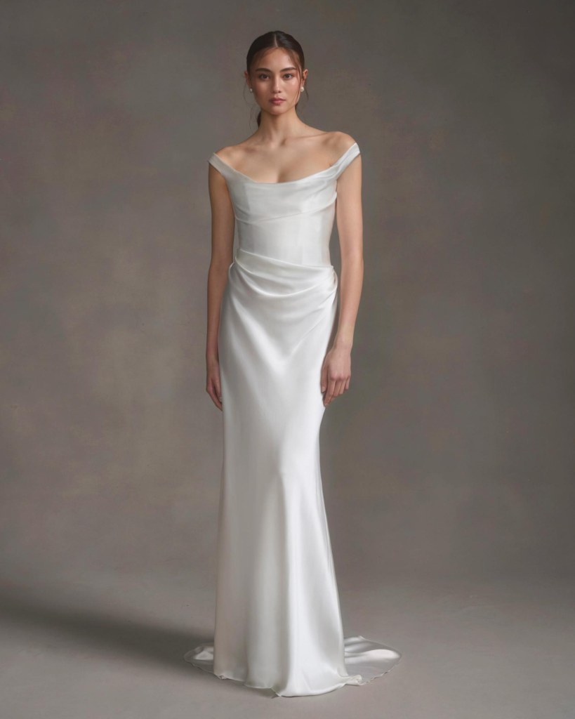 Dökümlü saten kumaştan, off-shoulder yakalı minimal gelinlik giyen model – zarif ve modern gelinlik silüeti.