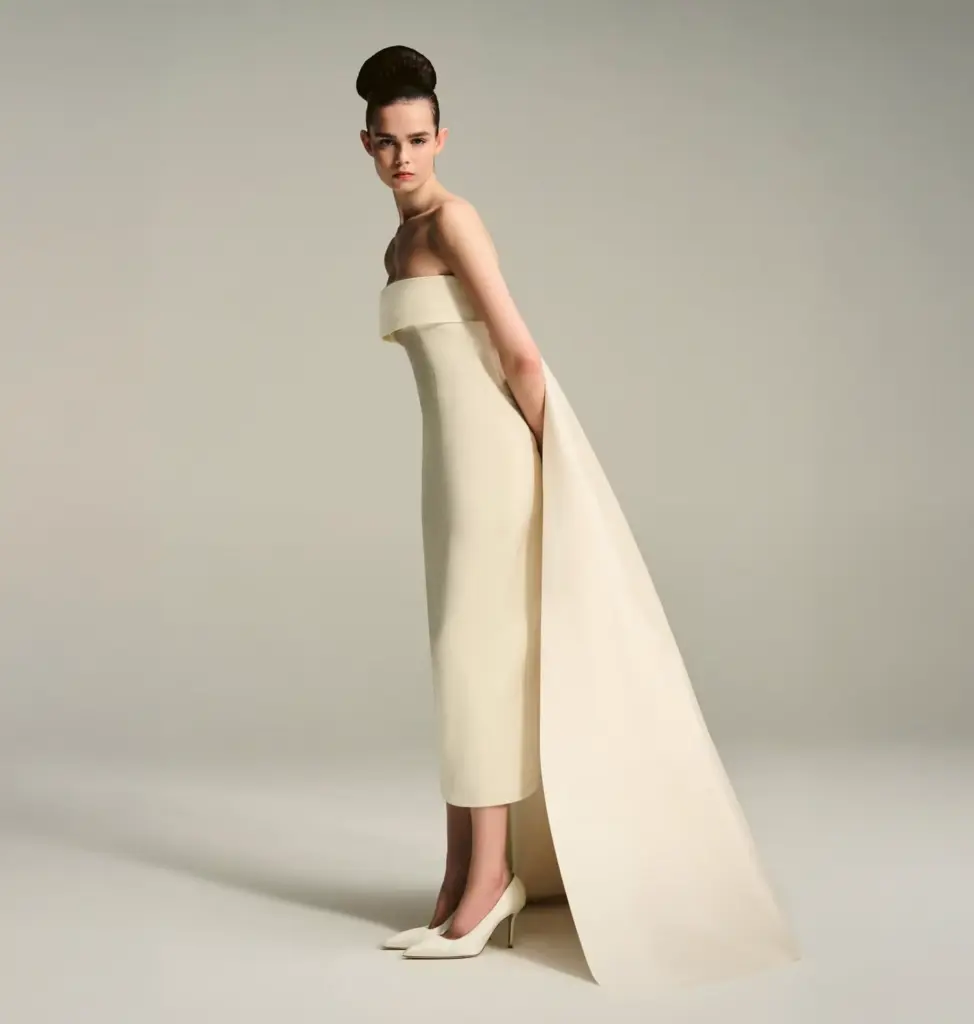 Straplez kesim, uzun kuyruk detaylı modern minimal gelinlik giyen modelin stüdyo çekimi; sade ve heykelsi düğün modası.