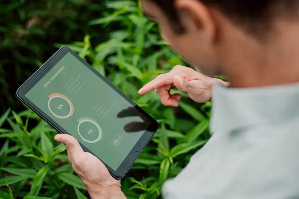 Yeşil bitkiler arasında tablet üzerinden sürdürülebilirlik verilerini analiz eden iş profesyoneli; ekonomi, yeşil finans ve çevresel performans ölçümü odaklı dijital değerlendirme.