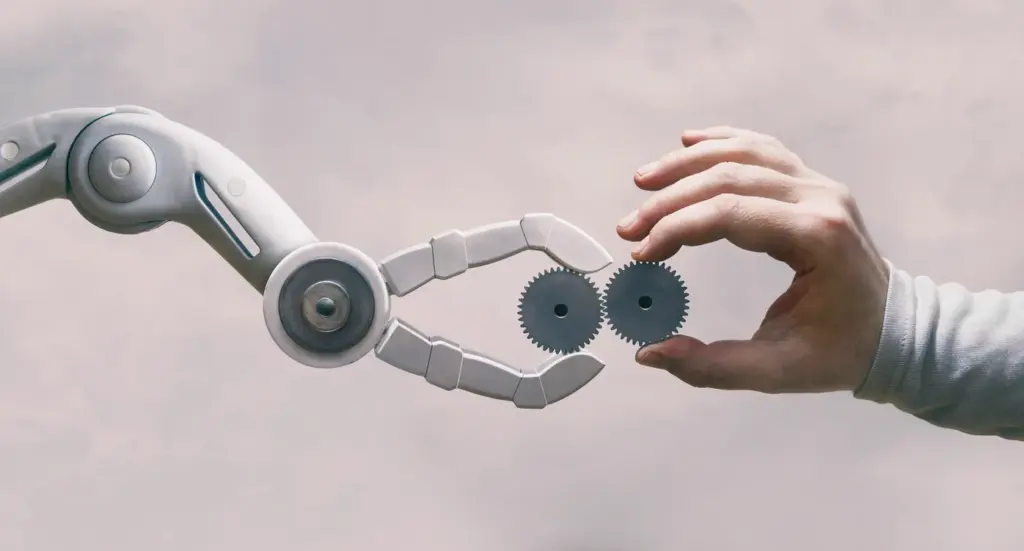 Bir robot kolu ve insan elinin iki dişliyi birlikte tuttuğu sahne; insan–makine iş birliği, yeniden beceri kazanımı ve 2026 iş gücü dönüşümü ve 2026 iş dünyası trendleri temsili.