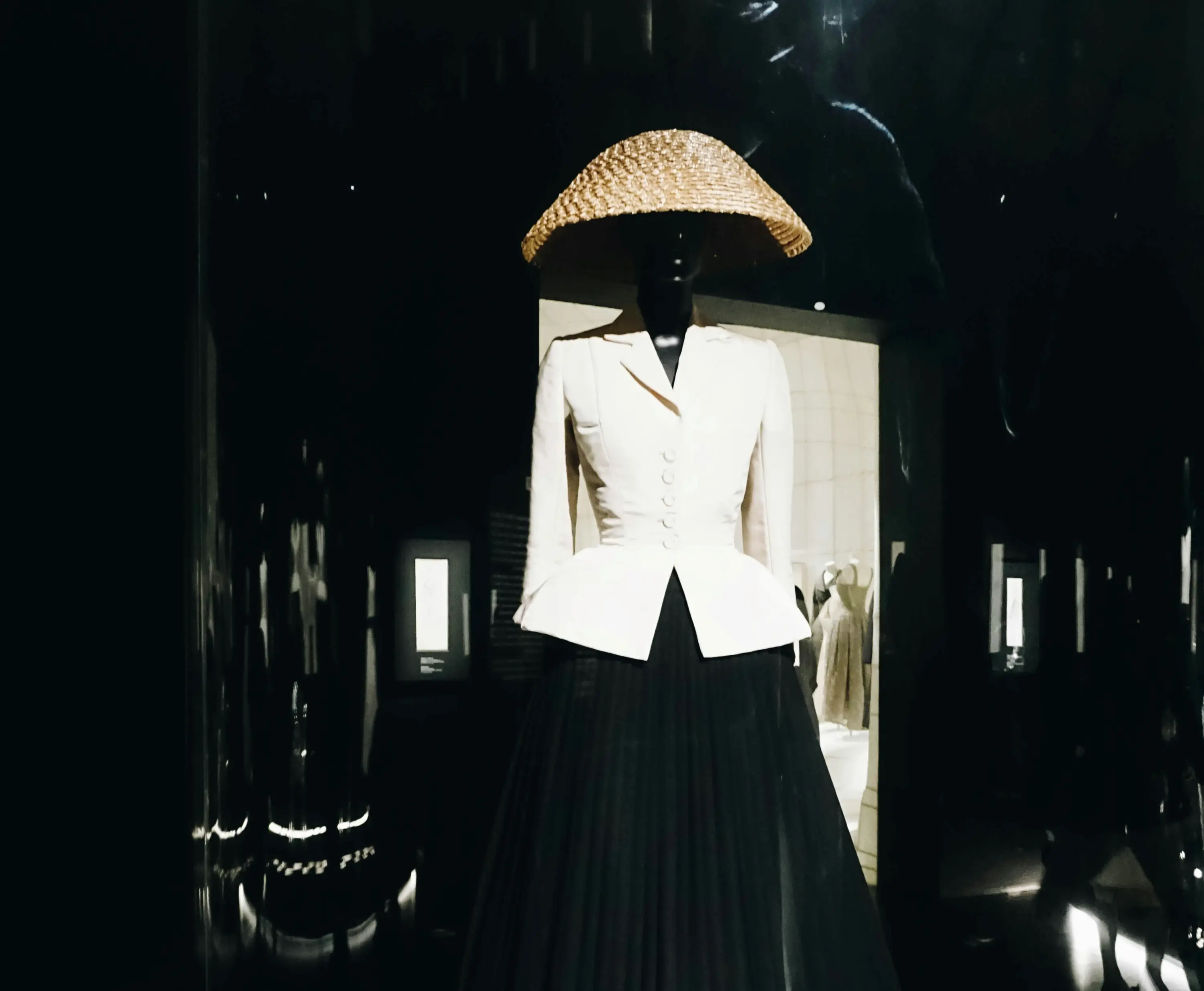 Couture esintili beyaz ceket tasarımının büyük hasır şapka ile sergilendiği minimalist moda vitrini görüntüsü.