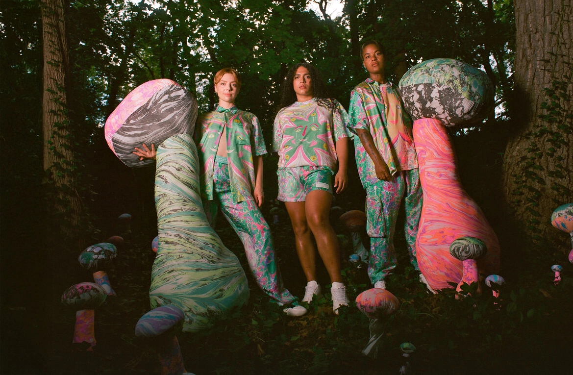 Stella McCartney’nin Unisex Gen Z koleksiyonunu yansıtan moda çekiminde, orman içinde renkli ve soyut desenli tasarımlar giyen üç modelin yer aldığı yaratıcı editorial sahne.