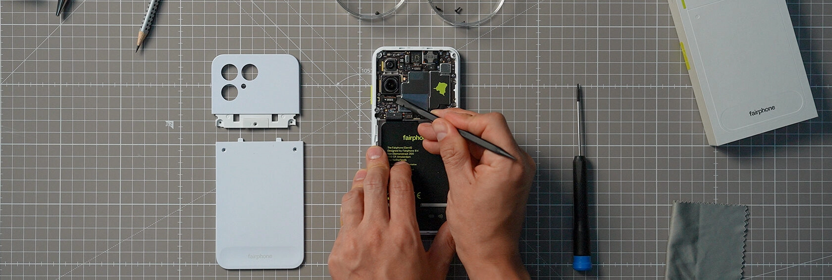 Fairphone modüler akıllı telefonun bir kullanıcı tarafından kolayca sökülüp tamir edildiğini gösteren çalışma alanı; çıkarılabilir arka kapak, kamera modülü, batarya ve onarım araçları düzenli bir şekilde masaya yerleştirilmiş.
