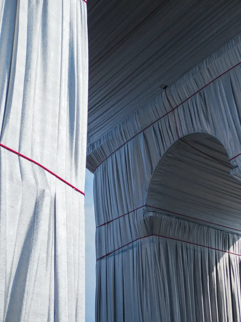 Christo ve Jeanne-Claude’un ‘Wrapped Arc de Triomphe’ projesinde yapı üzerini kaplayan gümüş gri kumaşın ve kırmızı iplerin mimari detaylarını gösteren yakın plan fotoğraf.