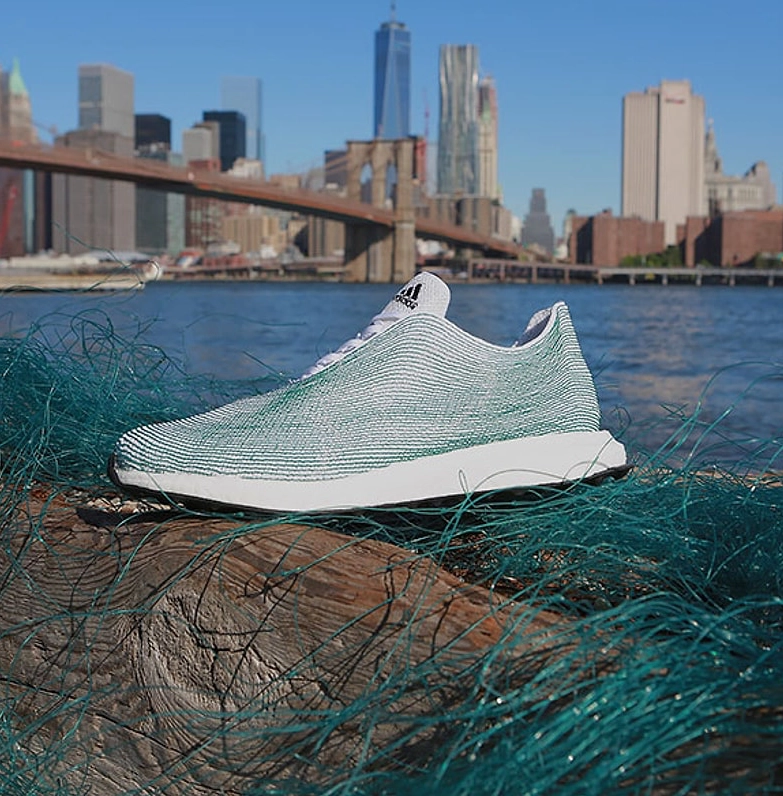Geri dönüştürülmüş okyanus plastiklerinden üretilen Adidas koşu ayakkabısının New York’ta Brooklyn Köprüsü manzarasıyla sergilendiği sürdürülebilir tasarım fotoğrafı.