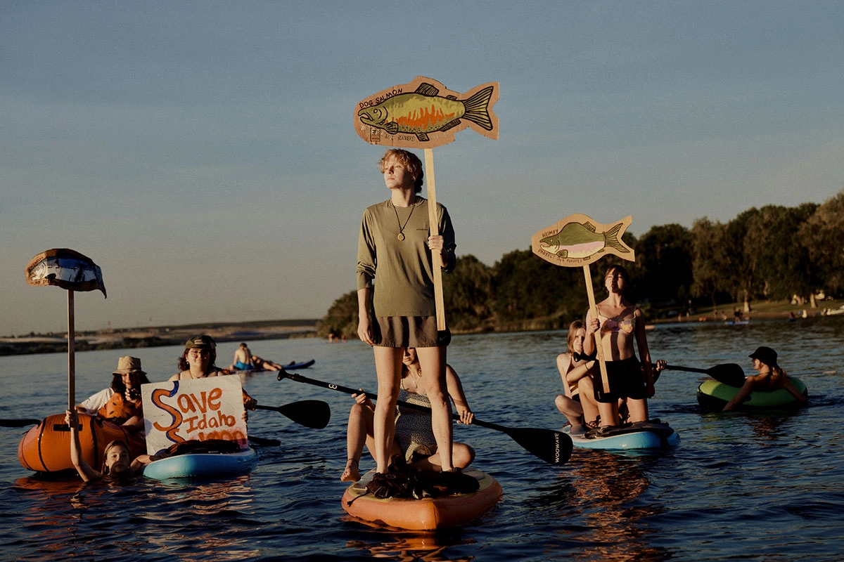 Gölde paddleboard ve botlarla ilerleyen genç aktivistlerin, balık figürlü pankartlar ve “Save Idaho Salmon” yazılı posterlerle çevre ve yaban hayatı koruma protestosu yapması.
