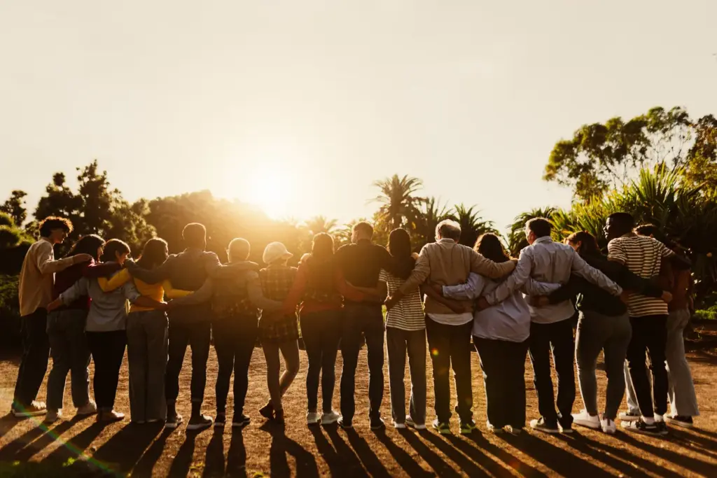 Kapsayıcı kurum kültürünü ve topluluk wellbeing yaklaşımını temsil eden gün batımı sırasında birlikte duran geniş bir kalabalık.