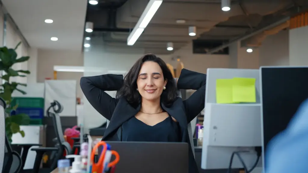 Ofiste omuzlarını gevşetip rahatlama egzersizi yapan kadın çalışan.