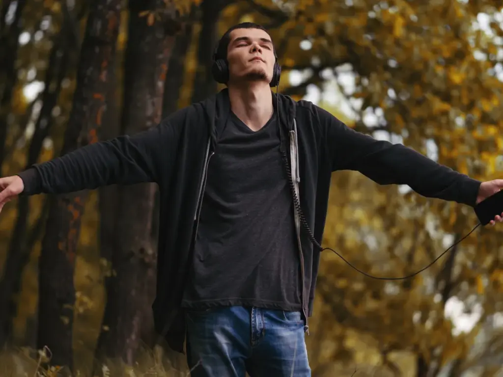 2026 wellbeing trendlerinde öne çıkan mindfulness’ı temsil eden kulaklıkla ormanda meditasyon yapan genç erkek.