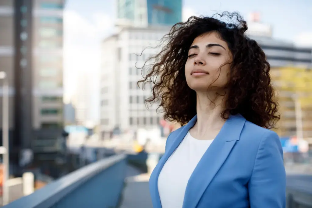 Çalışan wellbeing yatırımının çok yönlü faydalarını temsil eden dış mekânda gözleri kapalı rahatlayan kadın portresi.